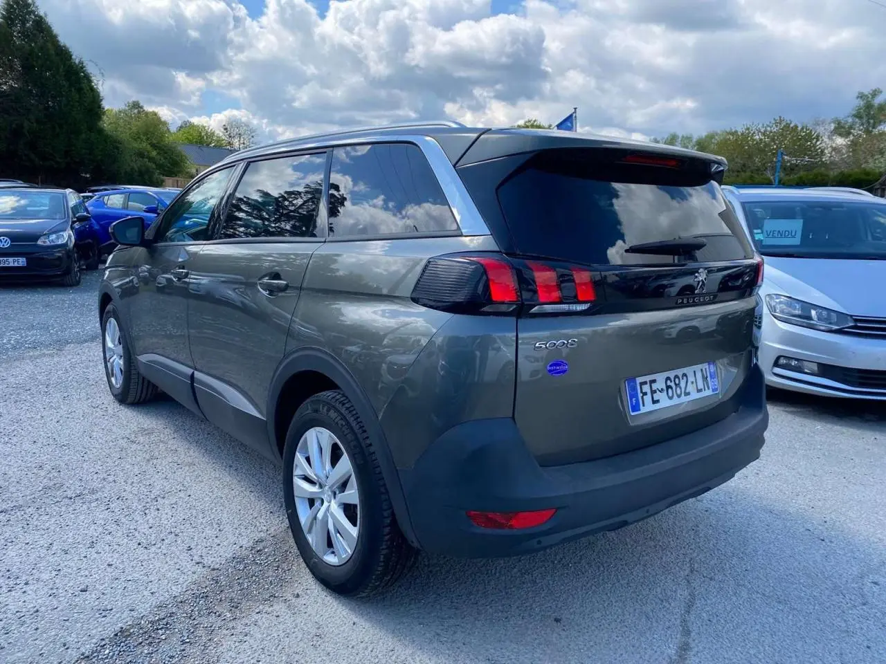 Peugeot 5008 gris clair vue 3/4 arrière droit, vitres surteintées et feux arrière à griffes rouges.