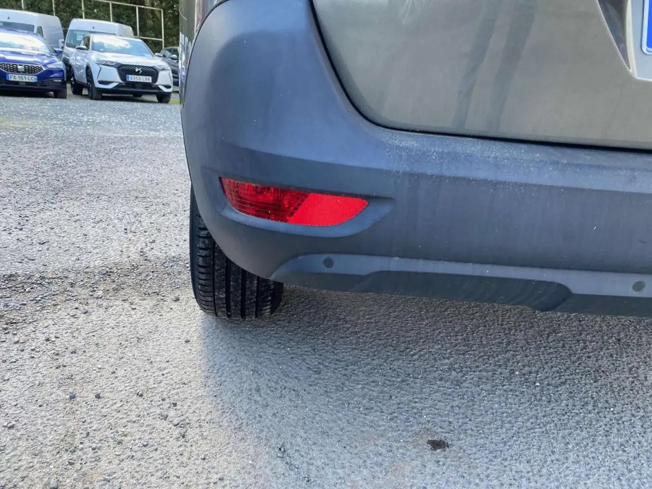 Gros plan sur le pare-chocs arrière gris clair du Peugeot 5008 avec feu rouge et capteurs de recul visibles.