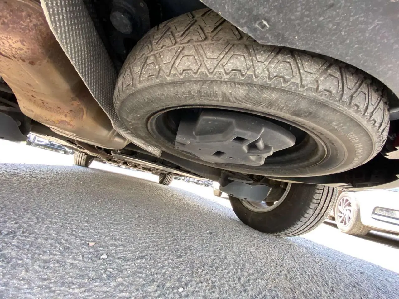Vue en contre-plongée sous un Peugeot 5008 gris clair, mettant en valeur la roue de secours galette sous le véhicule.