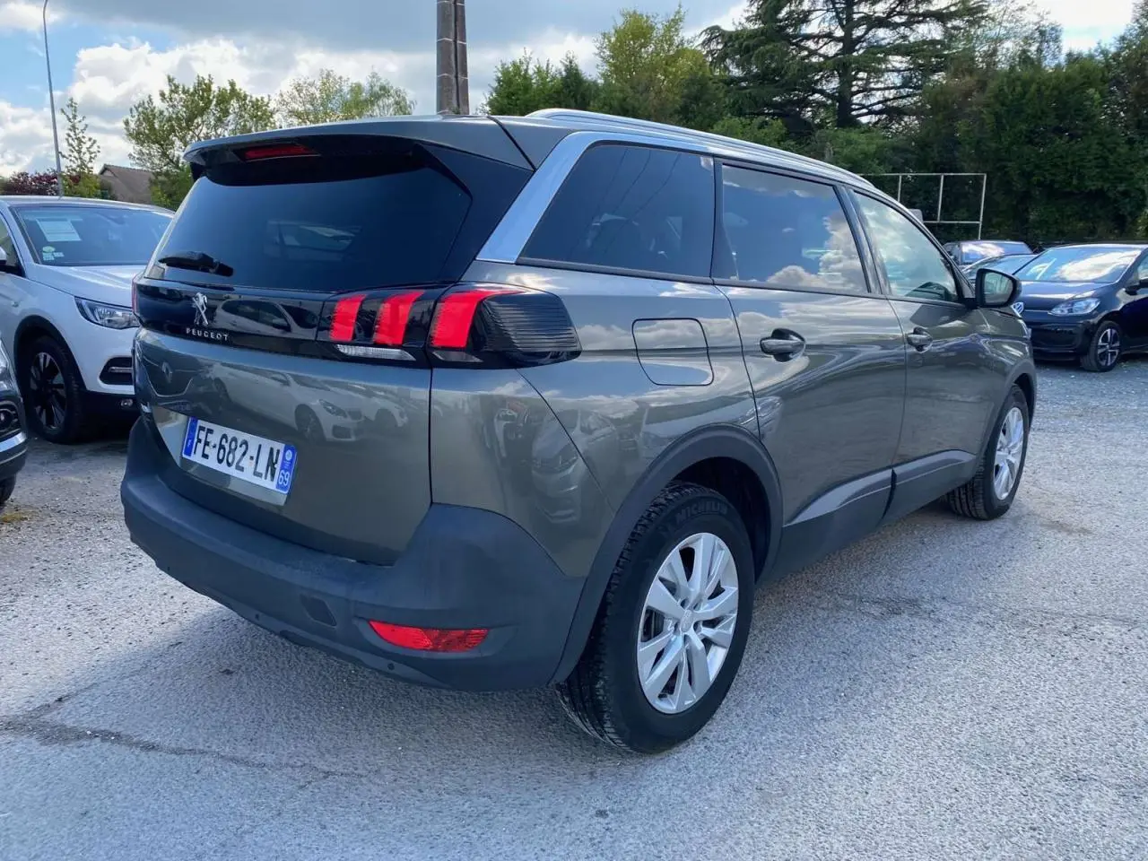 Peugeot 5008 gris clair vue 3/4 arrière droit, feux arrière à griffes rouges et vitres surteintées.