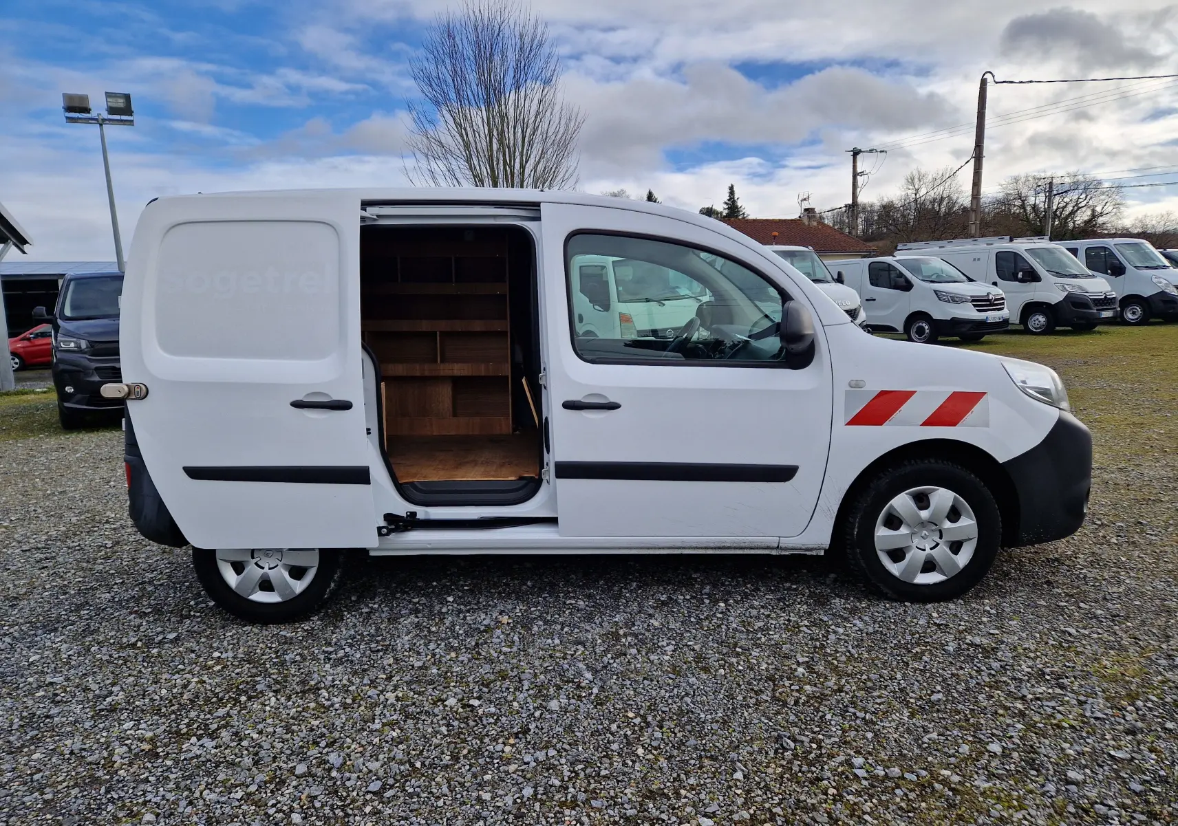 Vue de profil droit d’un Renault Kangoo blanc 2020 avec porte latérale coulissante ouverte montrant l’aménagement intérieur en bois.