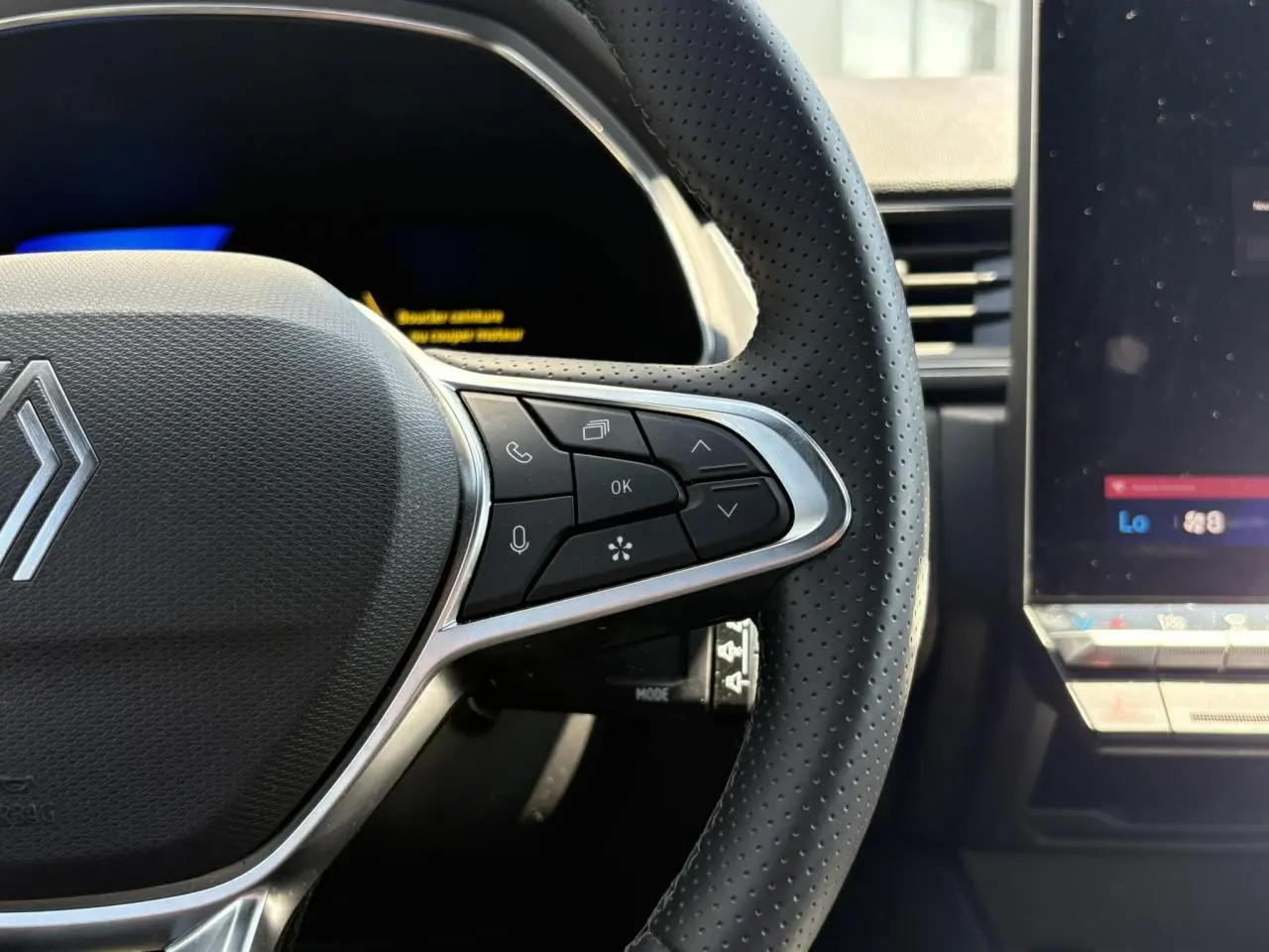 Gros plan sur le côté droit du volant perforé noir du Renault Symbioz 2025 avec commandes intégrées et écran tactile adjacent.