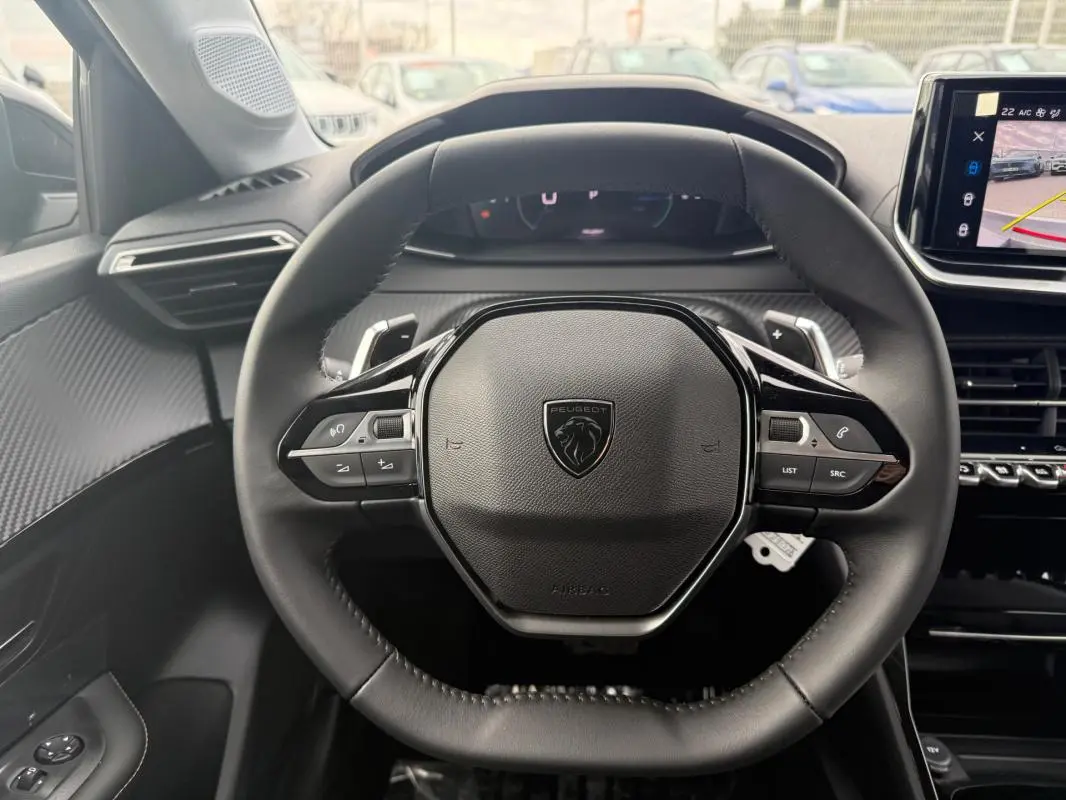 Vue rapprochée du volant noir de la Peugeot 208 Hybrid 145 Allure 2025 avec commandes intégrées et tableau de bord numérique.