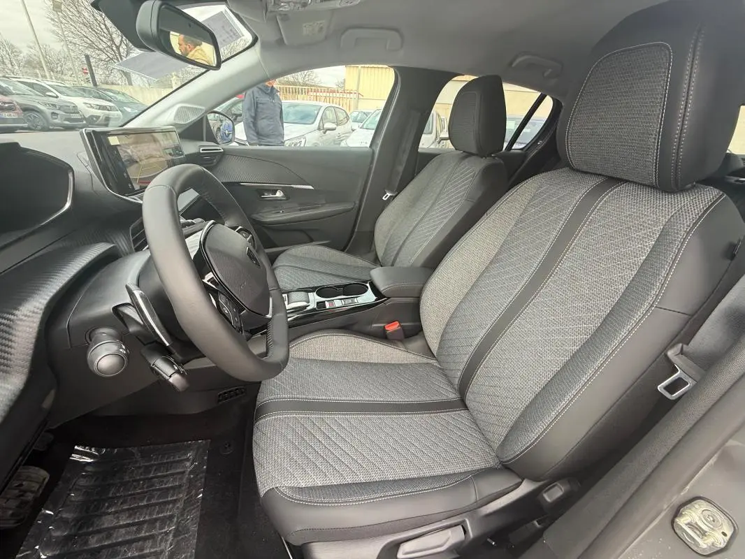 Vue intérieure côté conducteur de la Peugeot 208 Hybrid 145 gris, mettant en valeur les sièges tissu et le volant multifonction.