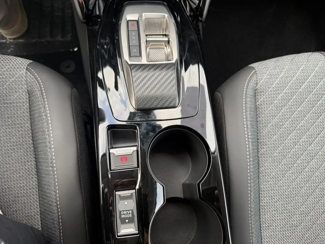 Vue plongeante sur la console centrale noire brillante de la Peugeot 208 Hybrid 145, avec levier de vitesses et porte-gobelets.