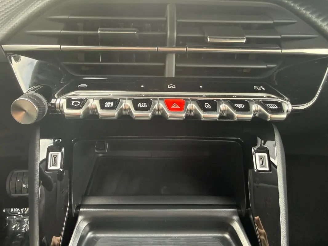 Vue rapprochée du tableau de bord de la Peugeot 208 Hybrid 145 Allure 2025, avec boutons de commande et finition noire brillante.