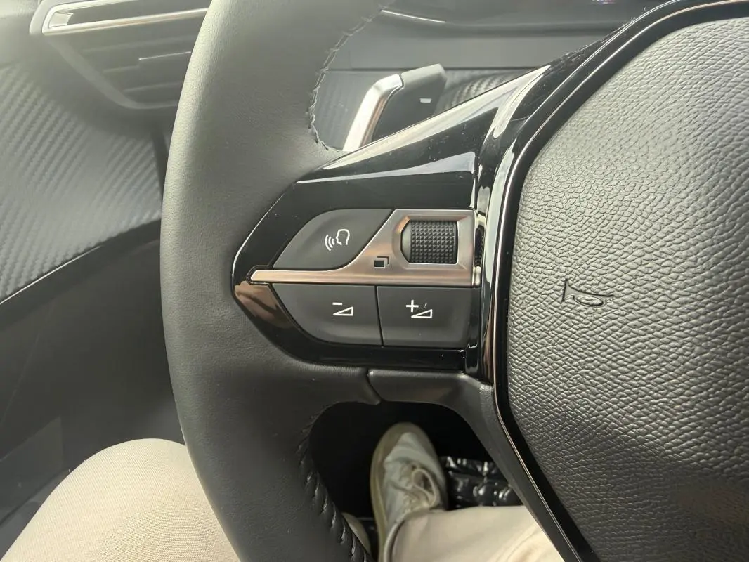 Gros plan sur les commandes gauche du volant noir du Peugeot 208 Hybrid 145 gris, avec bouton volume et Bluetooth.