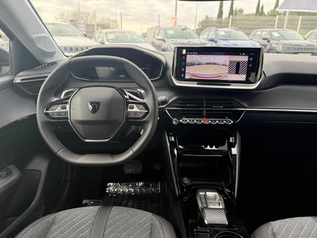 Vue intérieure avant de la Peugeot 208 Hybrid 145 Allure, volant cuir, écran tactile avec caméra de recul, sellerie grise.