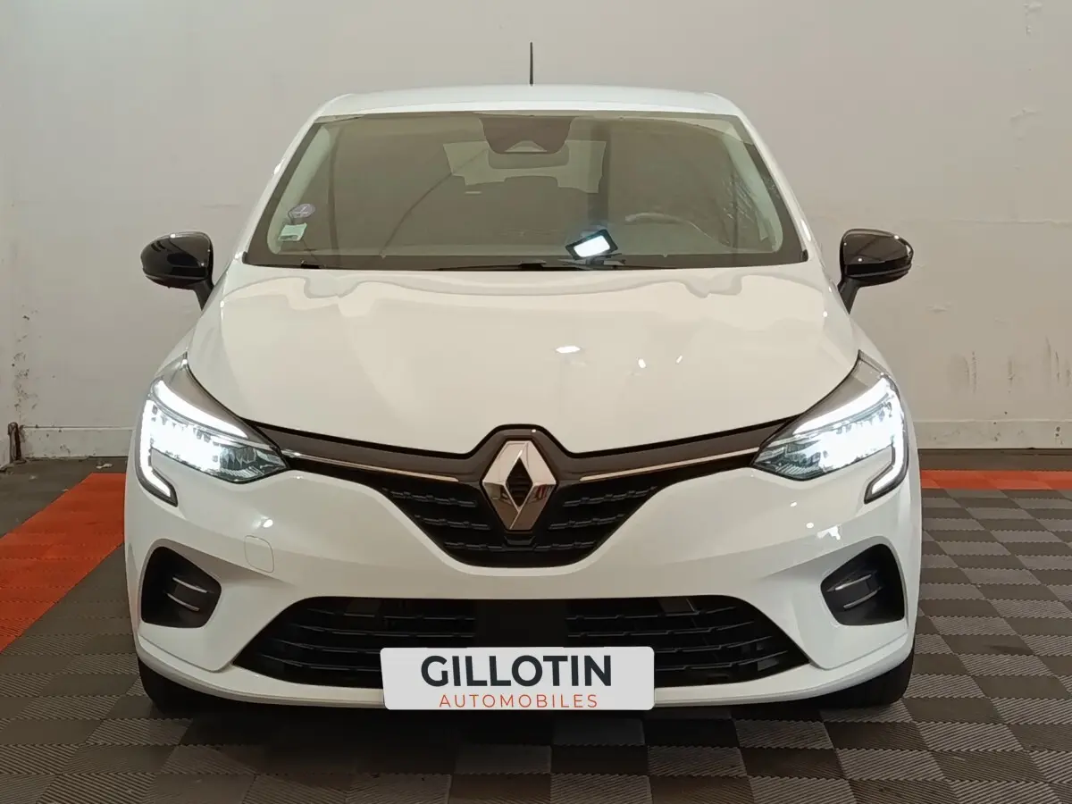 Vue avant d'une Renault Clio Evolution TCe 90 blanche avec phares LED allumés et rétroviseurs noirs.
