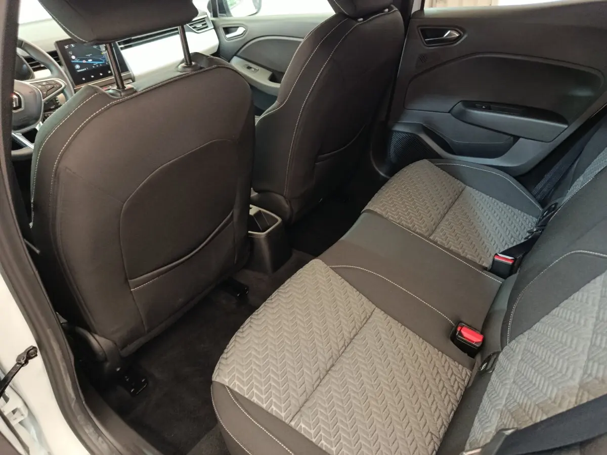 Vue intérieure arrière droite de la Renault Clio blanche 2023, sièges tissu gris à motifs et dossier avant noir.