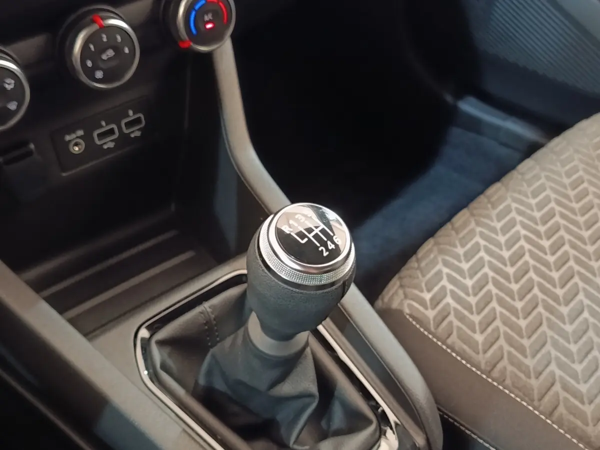 Gros plan sur le levier de vitesses manuel noir et argenté de la Renault Clio Evolution TCe 90, avec siège tissu gris à motifs.