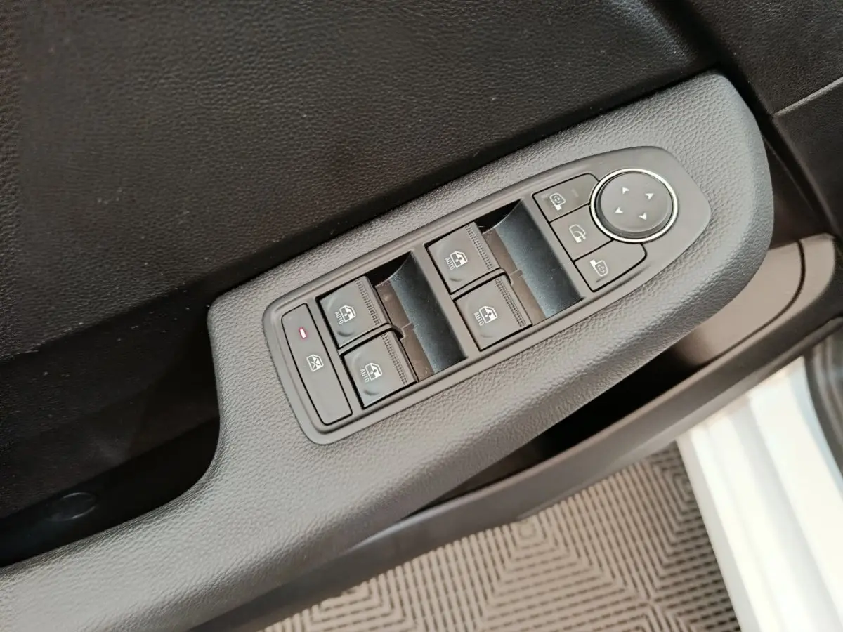 Vue rapprochée des commandes de lève-vitres et rétroviseurs sur la porte côté conducteur d’une Renault Clio blanche 2023.