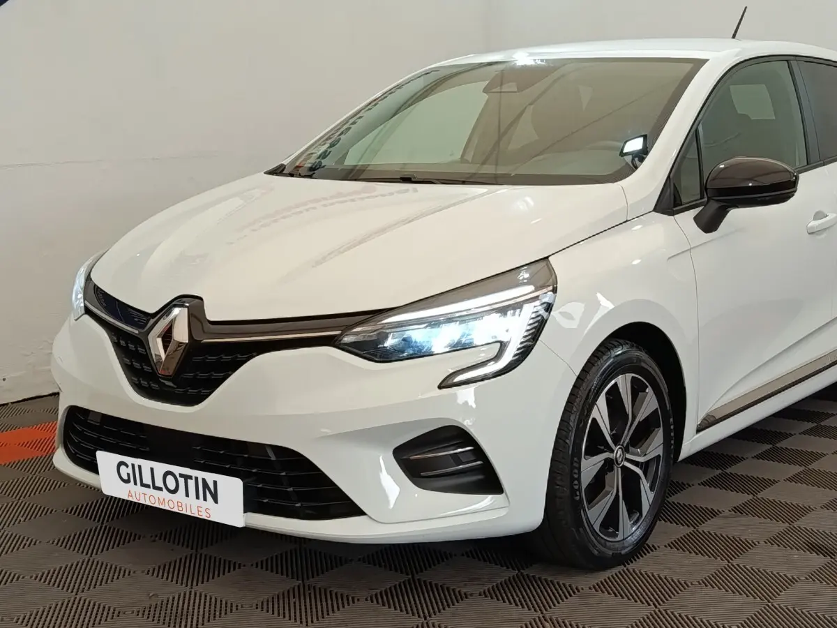 Renault Clio Evolution TCe 90 blanche vue en 3/4 avant droit avec phares LED allumés et jantes alliage noires.