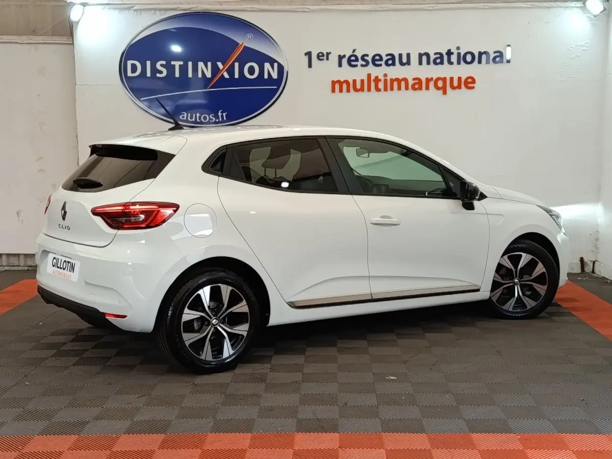 Profil droit d'une Renault Clio Evolution TCe 90 blanche 2023 avec jantes alliage et vitres teintées, en intérieur showroom.