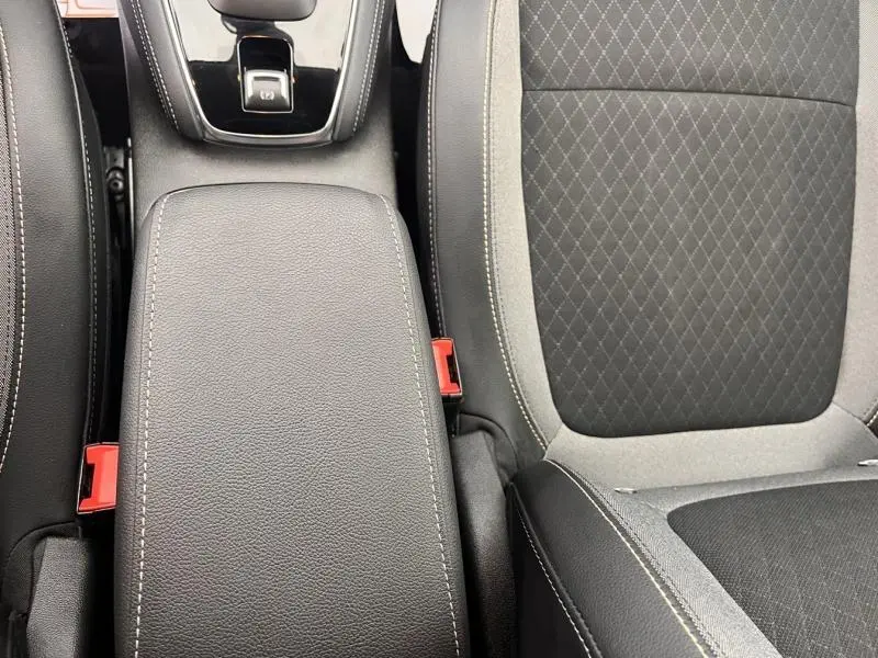 Vue rapprochée de l'accoudoir central en cuir noir avec surpiqûres blanches et siège tissu gris et noir de l'Opel Grandland 2023.