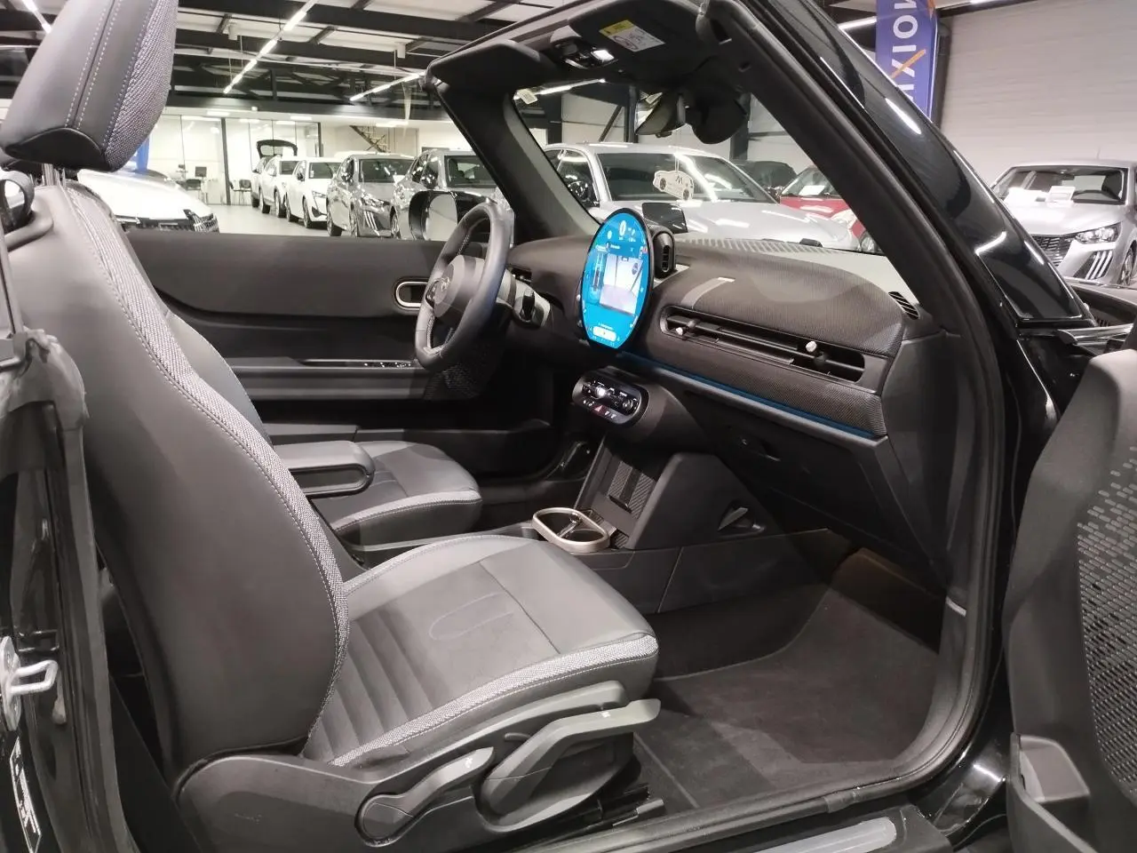 Vue intérieure côté passager d'une MINI Cabriolet noire 2025 avec tableau de bord moderne et sièges similicuir perforé.
