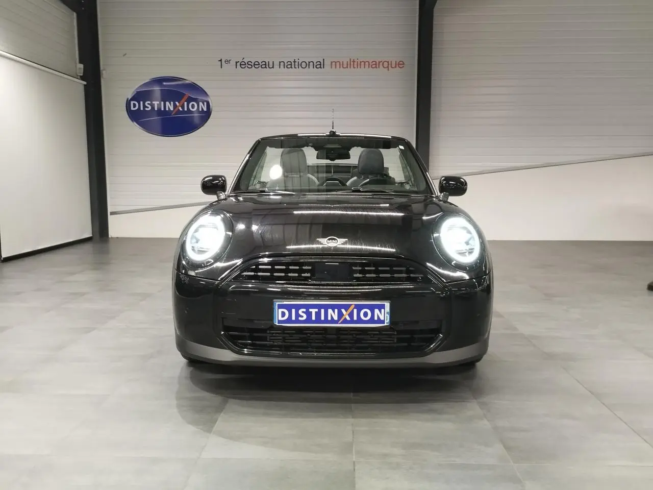 Vue avant d'une MINI Cabriolet noire 2025 avec phares LED allumés dans un showroom.