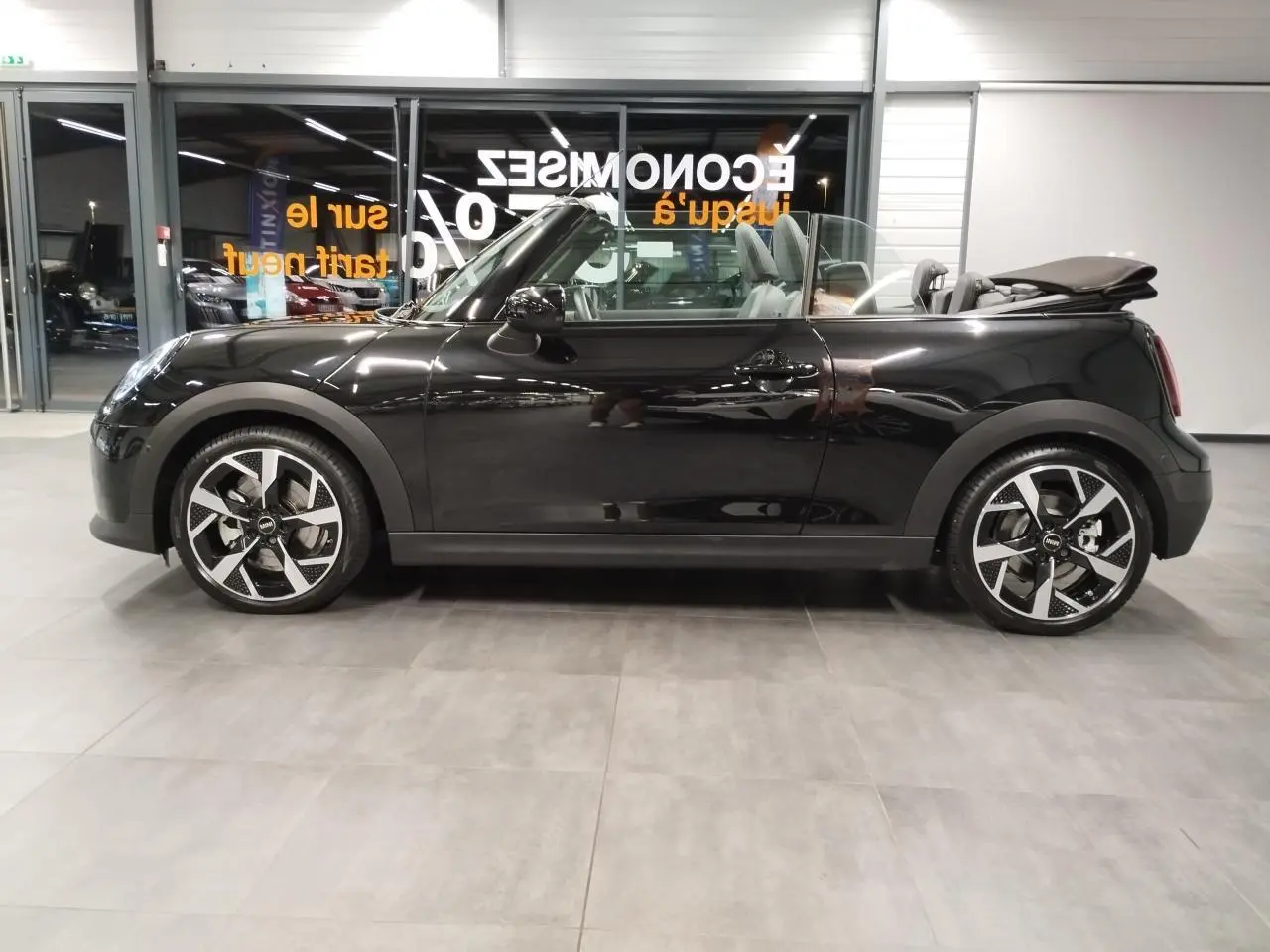 Vue de profil côté gauche d'un cabriolet MINI Cooper C Classic noir avec capote ouverte et jantes 16 pouces design 4-Square Spoke.