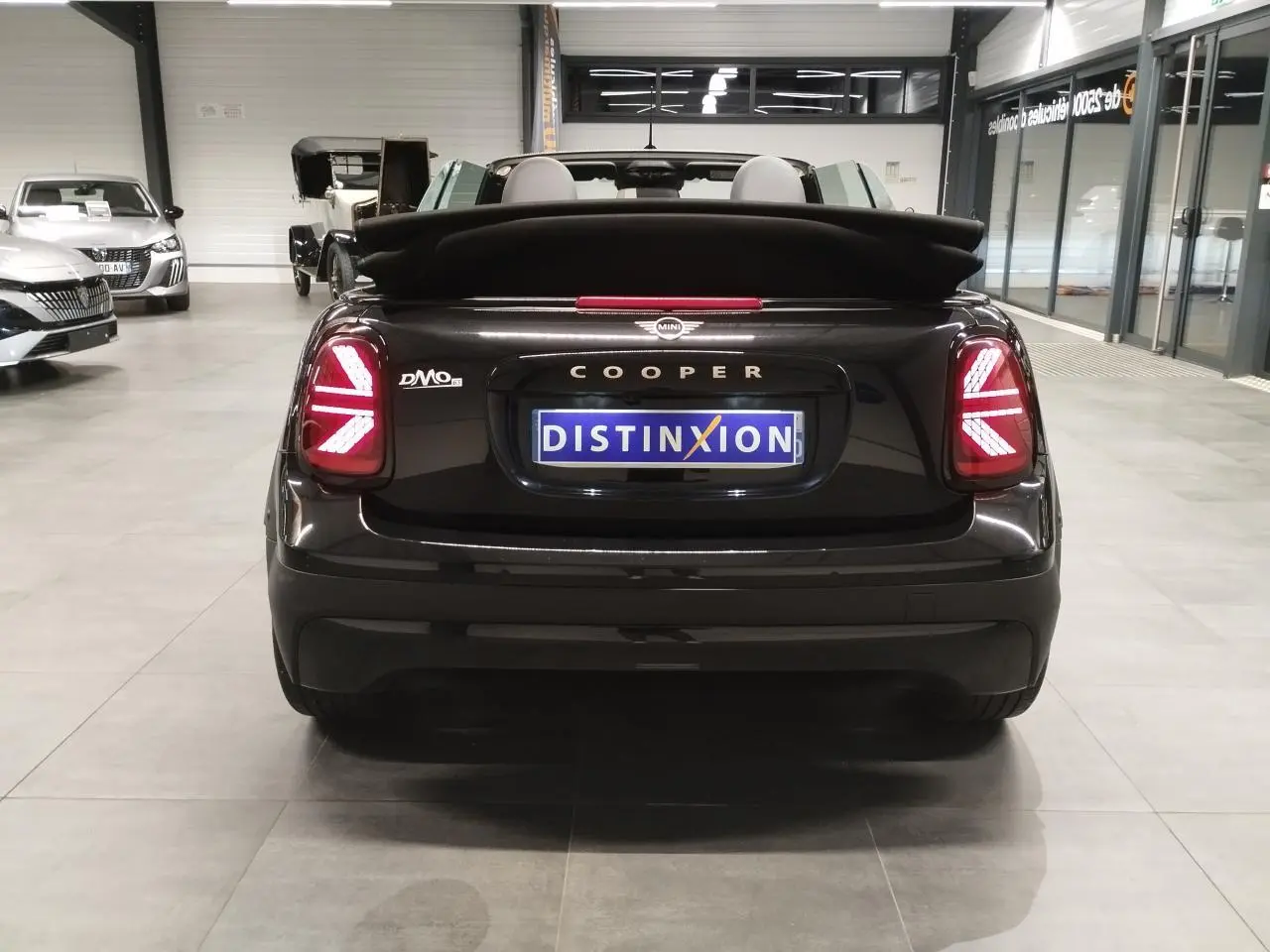 Vue arrière d'une MINI Cooper Cabriolet noire 2025 avec feux arrière LED en motif Union Jack et capote repliée.