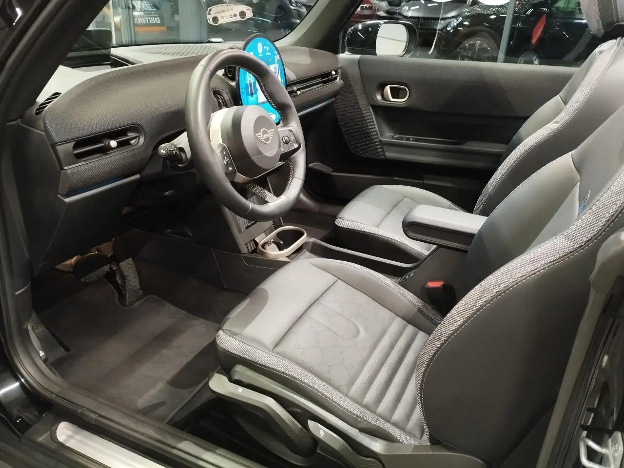 Vue intérieure côté conducteur de la MINI Cabriolet noire 2025, avec sièges sport gris et tableau de bord moderne.