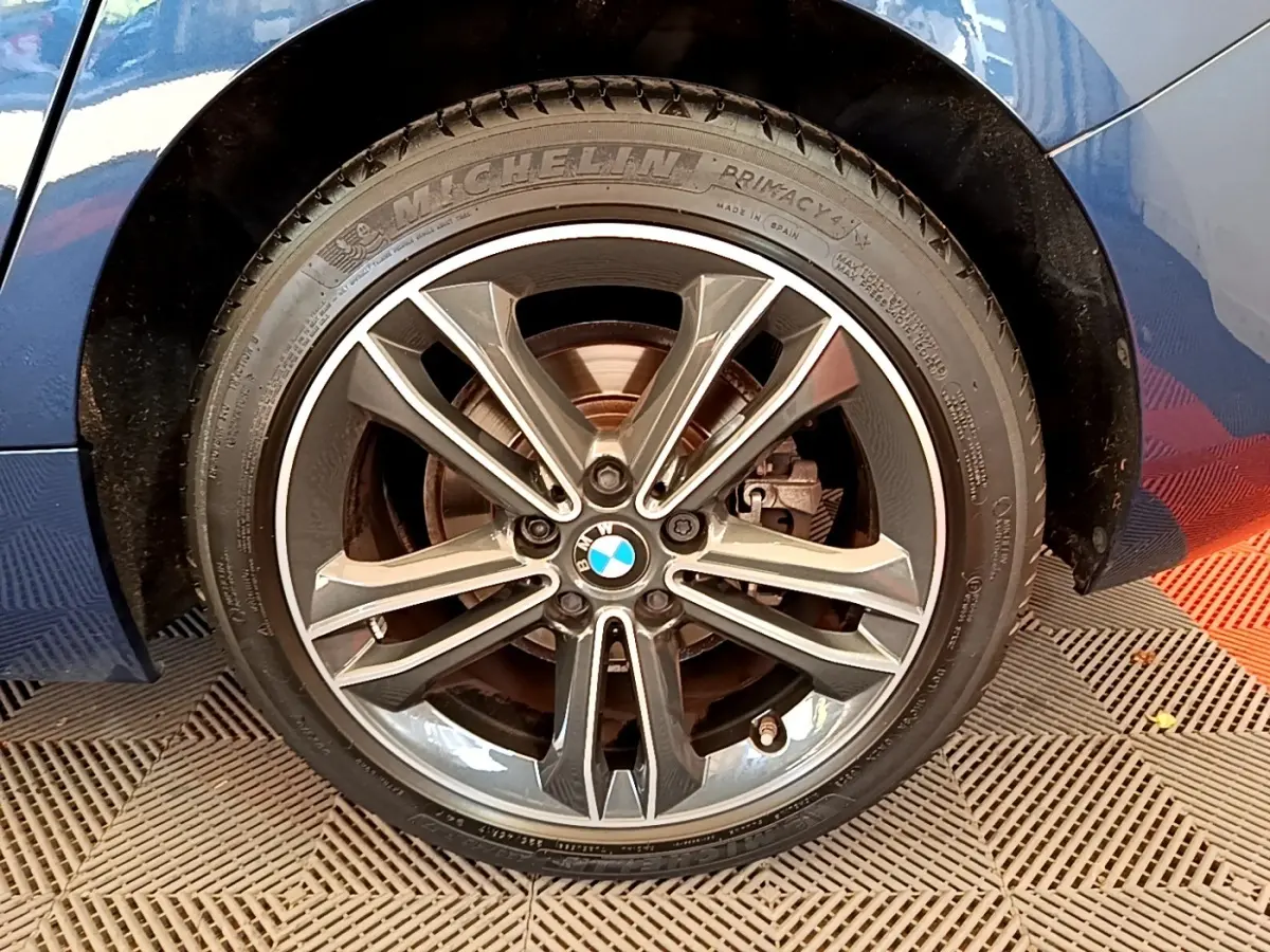 Gros plan sur la roue avant droite d’une BMW Série 1 118i bleu avec jante alliage et pneu Michelin.