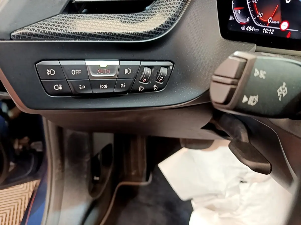 Gros plan sur les commandes d’éclairage et le volant côté gauche de la BMW Série 1 118i bleu 2023.