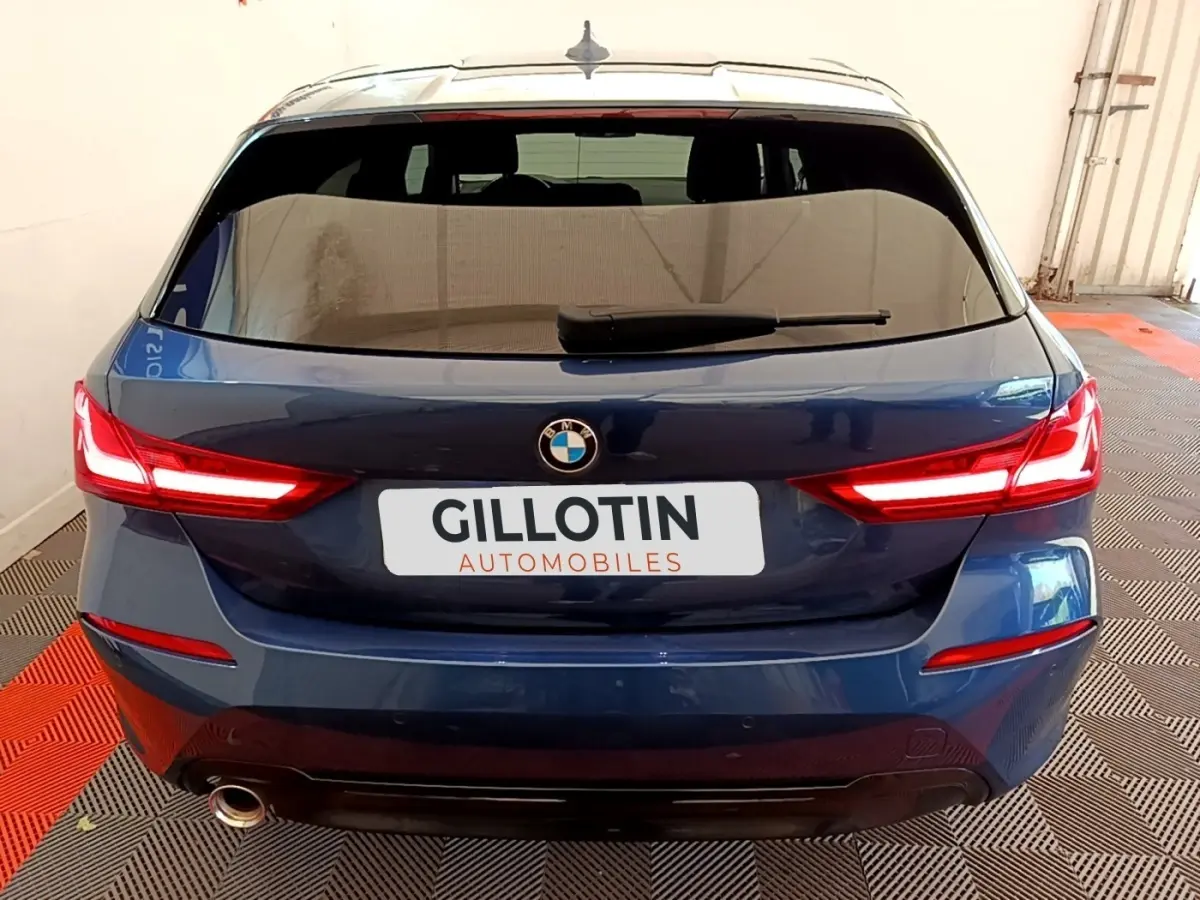Vue arrière d'une BMW Série 1 118i Edition Sport bleu, feux LED allumés et sortie d'échappement visible côté gauche.