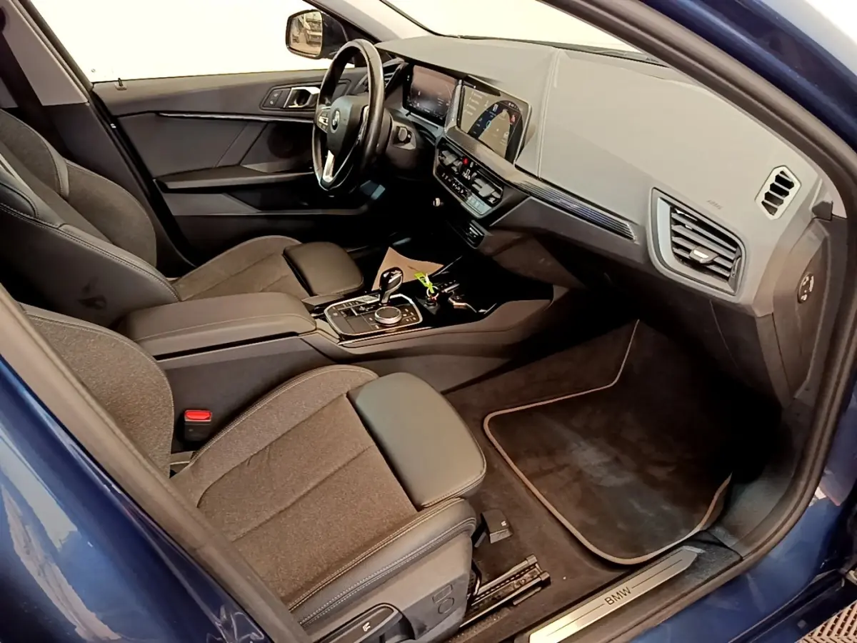 Intérieur BMW Série 1 118i bleu, vue côté passager avant, tableau de bord moderne avec écran tactile couleur.