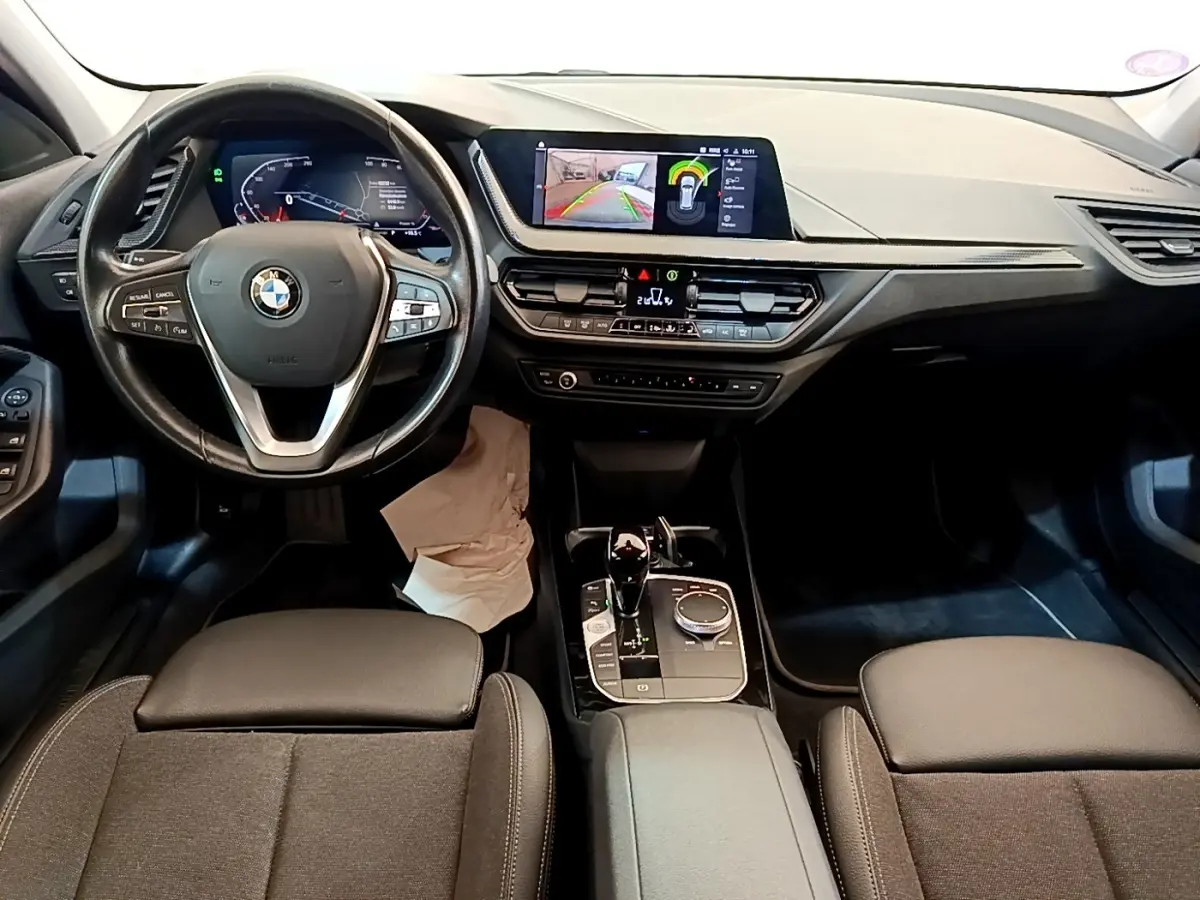 Vue intérieure avant de la BMW Série 1 118i Edition Sport 2023, tableau de bord avec écran tactile et volant multifonction.
