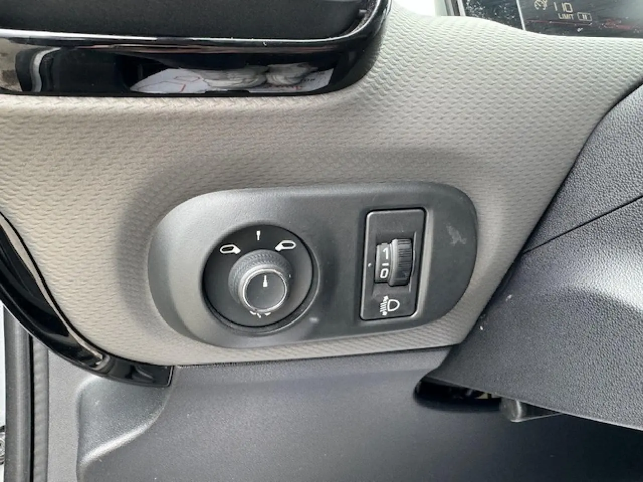 Gros plan sur les commandes d’éclairage et réglage des phares à gauche du tableau de bord d’une Citroën C4 Cactus gris clair 2020.