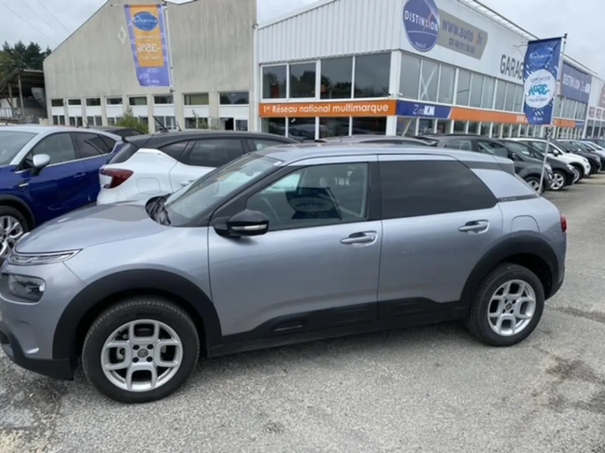 Profil côté gauche d'une Citroën C4 Cactus gris clair 2020 avec protections noires et jantes alliage au parking.