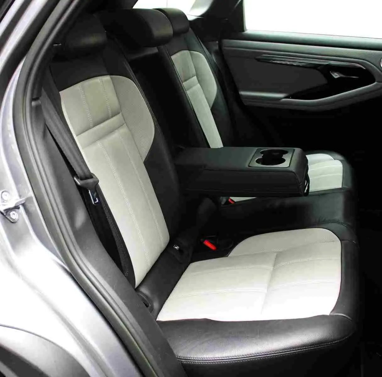 Vue intérieure côté gauche des sièges arrière bicolores noirs et gris du Range Rover Evoque 2023 gris métal avec accoudoir central rabattable.