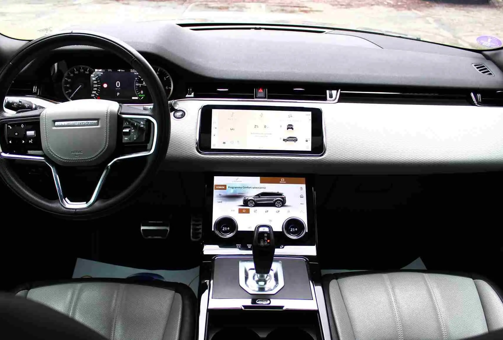 Range Rover Evoque gris métal 2023 en 3/4 avant droit, hybride rechargeable, devant un bâtiment commercial.