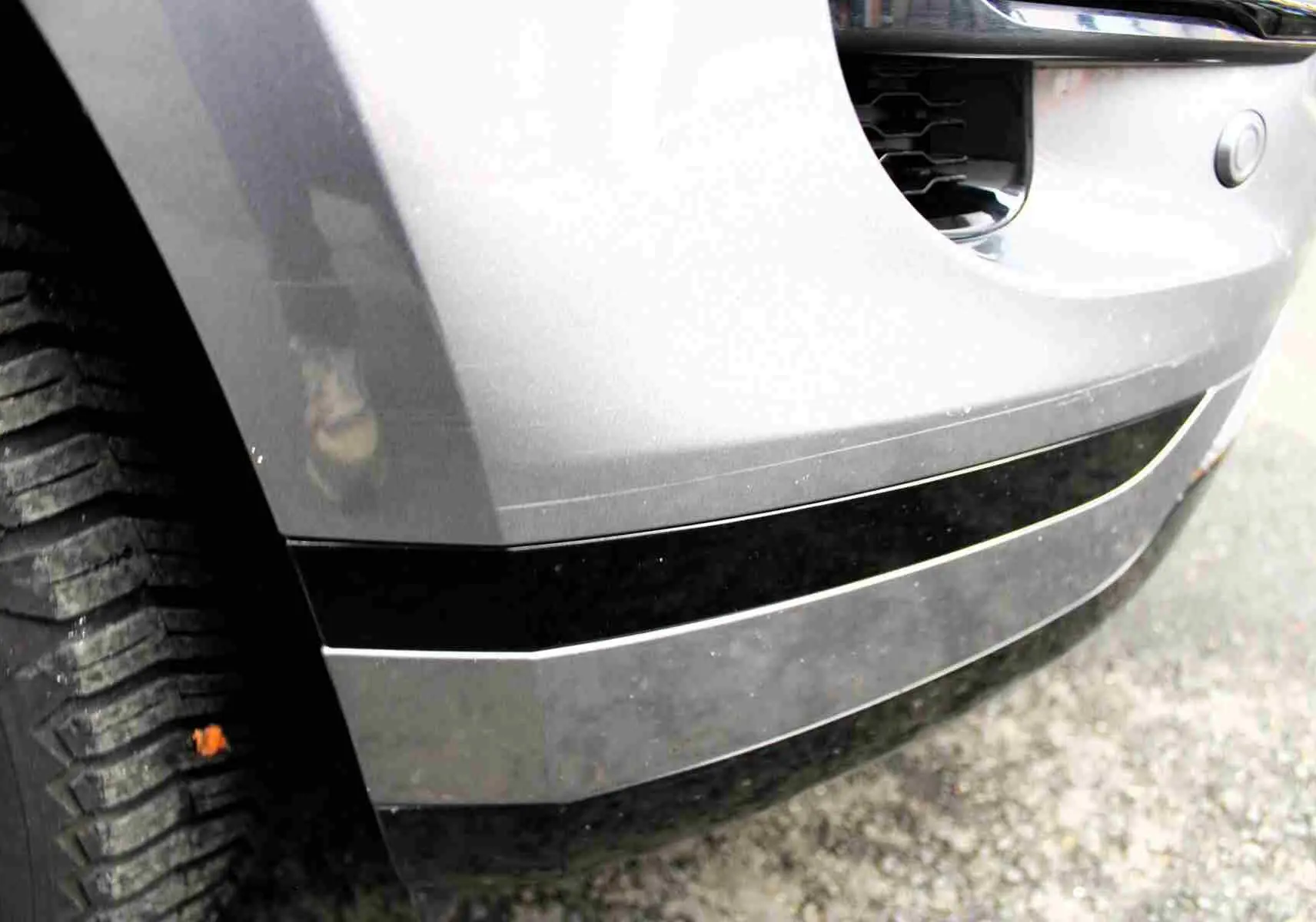 Gros plan sur l'angle avant gauche du Range Rover Evoque gris métal 2023, mettant en valeur le pare-chocs et la roue.