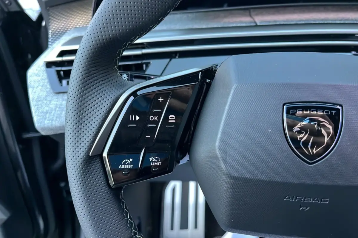 Gros plan sur le volant cuir perforé du Peugeot 5008 Hybrid 145 GT avec commandes multifonctions et logo lion noir.
