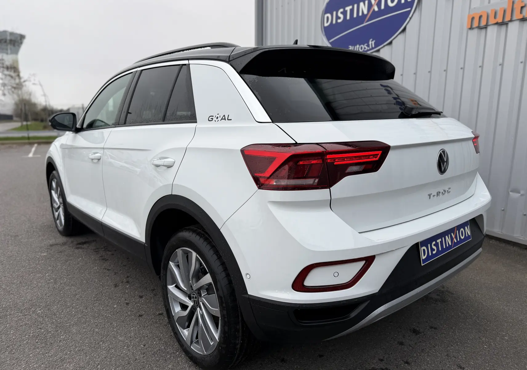Vue 3/4 arrière droite d’un Volkswagen T-Roc blanc Pure avec toit noir, feux arrière LED et jantes alliage.