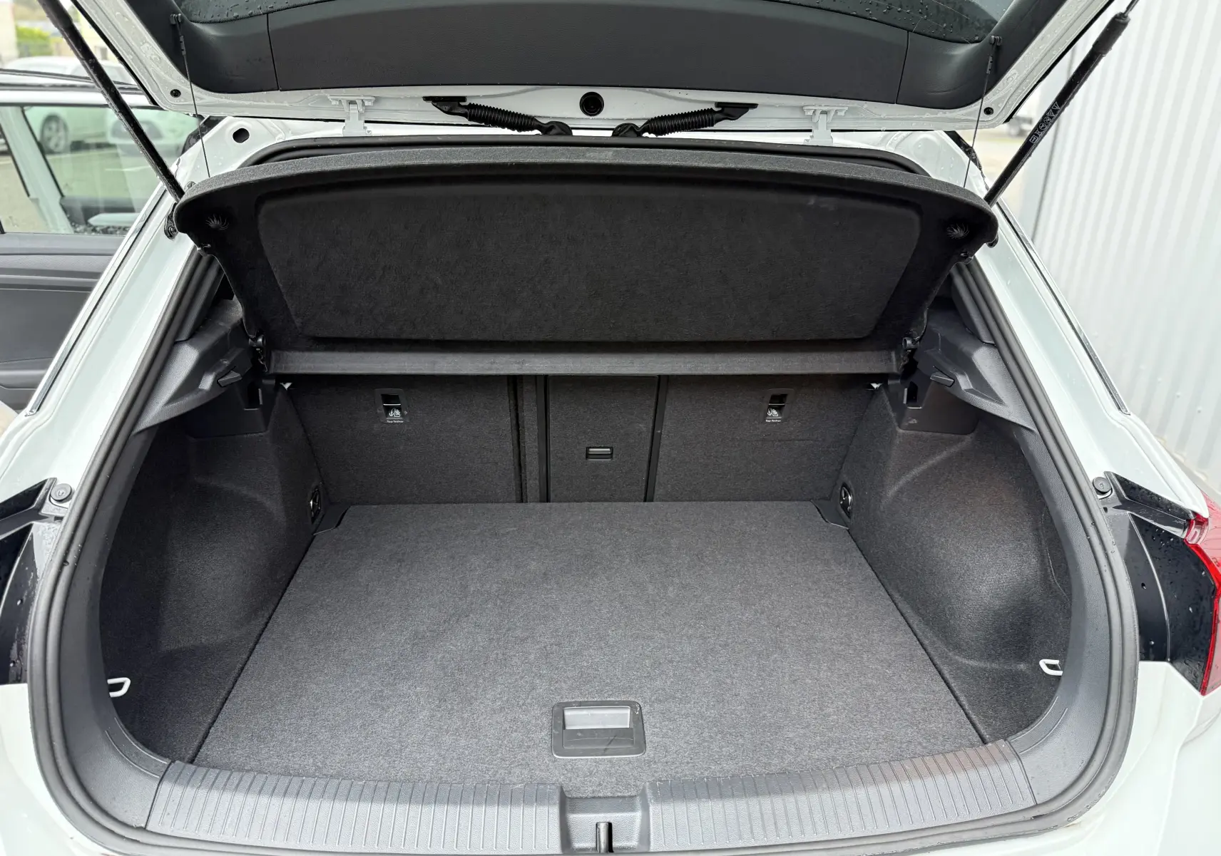 Coffre ouvert vu de l'arrière d'un Volkswagen T-Roc blanc pure avec toit noir, montrant un espace de chargement vide et propre.