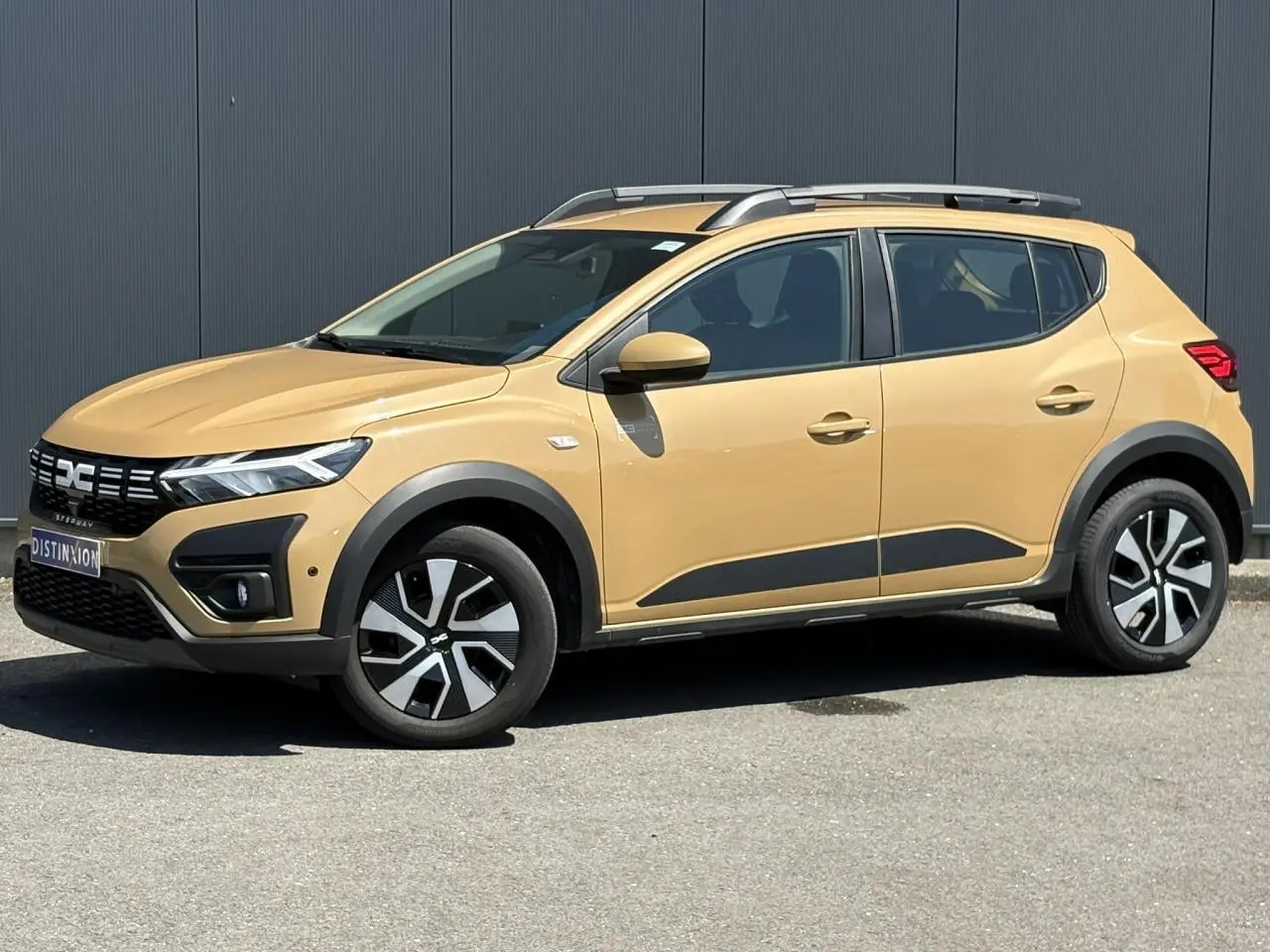 Vue latérale droite d'une Dacia Sandero Stepway beige Safari avec barres de toit et jantes distinctives.