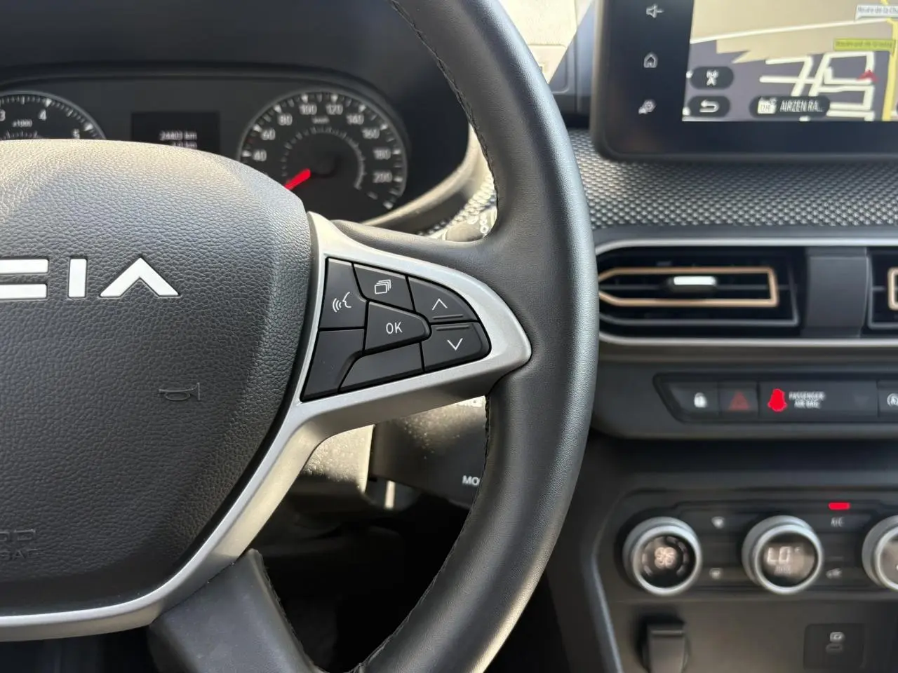 Gros plan sur le volant noir de la Dacia Sandero Stepway 2025 avec commandes multifonctions et écran tactile GPS visible.