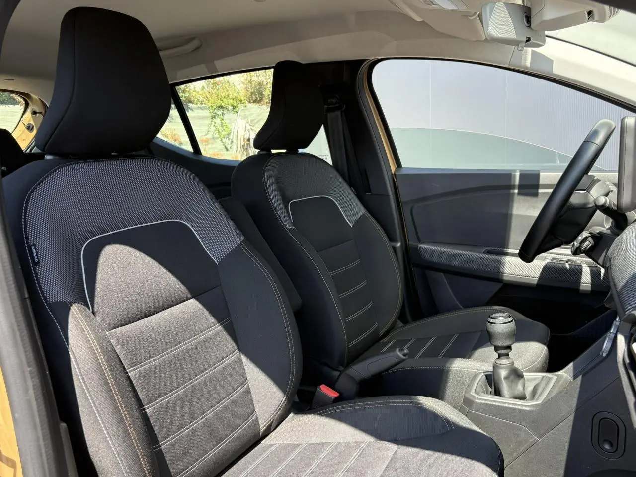Vue intérieure côté conducteur de la Dacia Sandero Stepway beige Safari, montrant les sièges et levier de vitesses manuel.