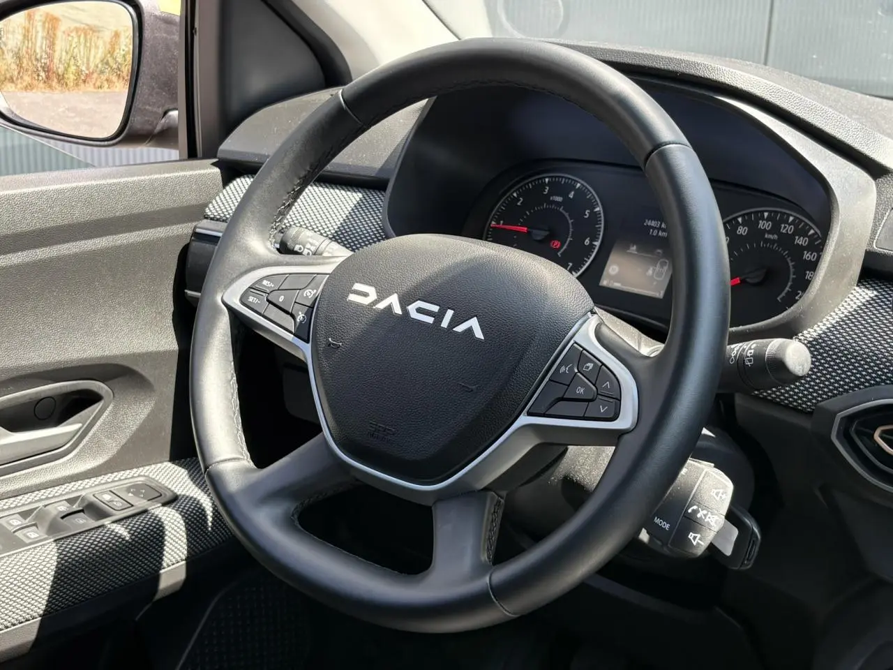 Vue intérieure centrée sur le volant noir Dacia avec tableau de bord et commandes au volant visibles.