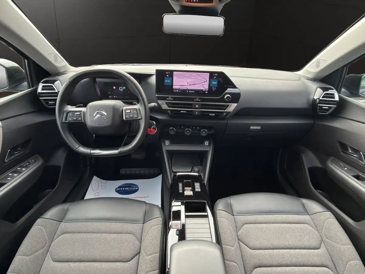 Vue intérieure avant de la Citroën C4 noire 2023, tableau de bord moderne avec écran tactile central et volant cuir multifonctions.