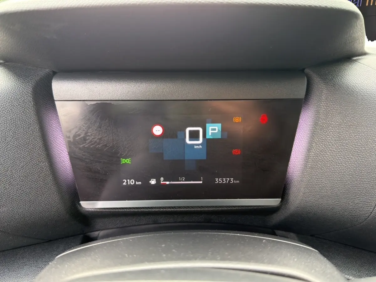 Affichage numérique du tableau de bord central de la Citroën C4 noir, montrant la vitesse à 0 km/h et l'autonomie restante.