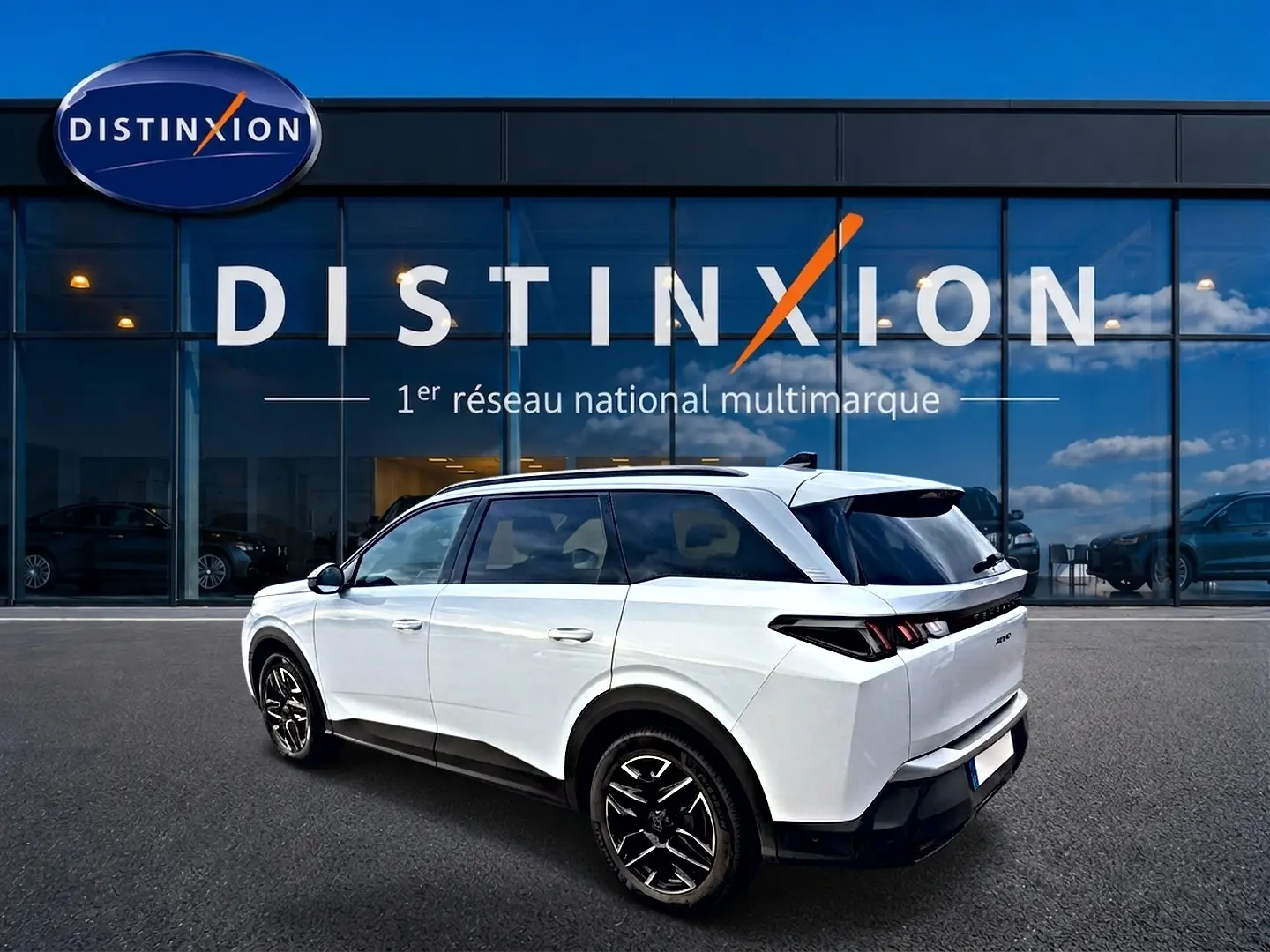 Peugeot 5008 blanc en 3/4 arrière droit, avec jantes alu noires et vitres arrière surteintées, devant une vitrine Distinxion.