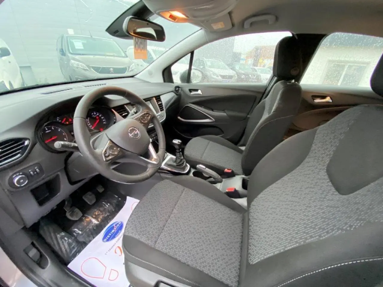 Vue intérieure côté conducteur de l'Opel Crossland gris, montrant le volant cuir, tableau de bord et sièges tissu gris.