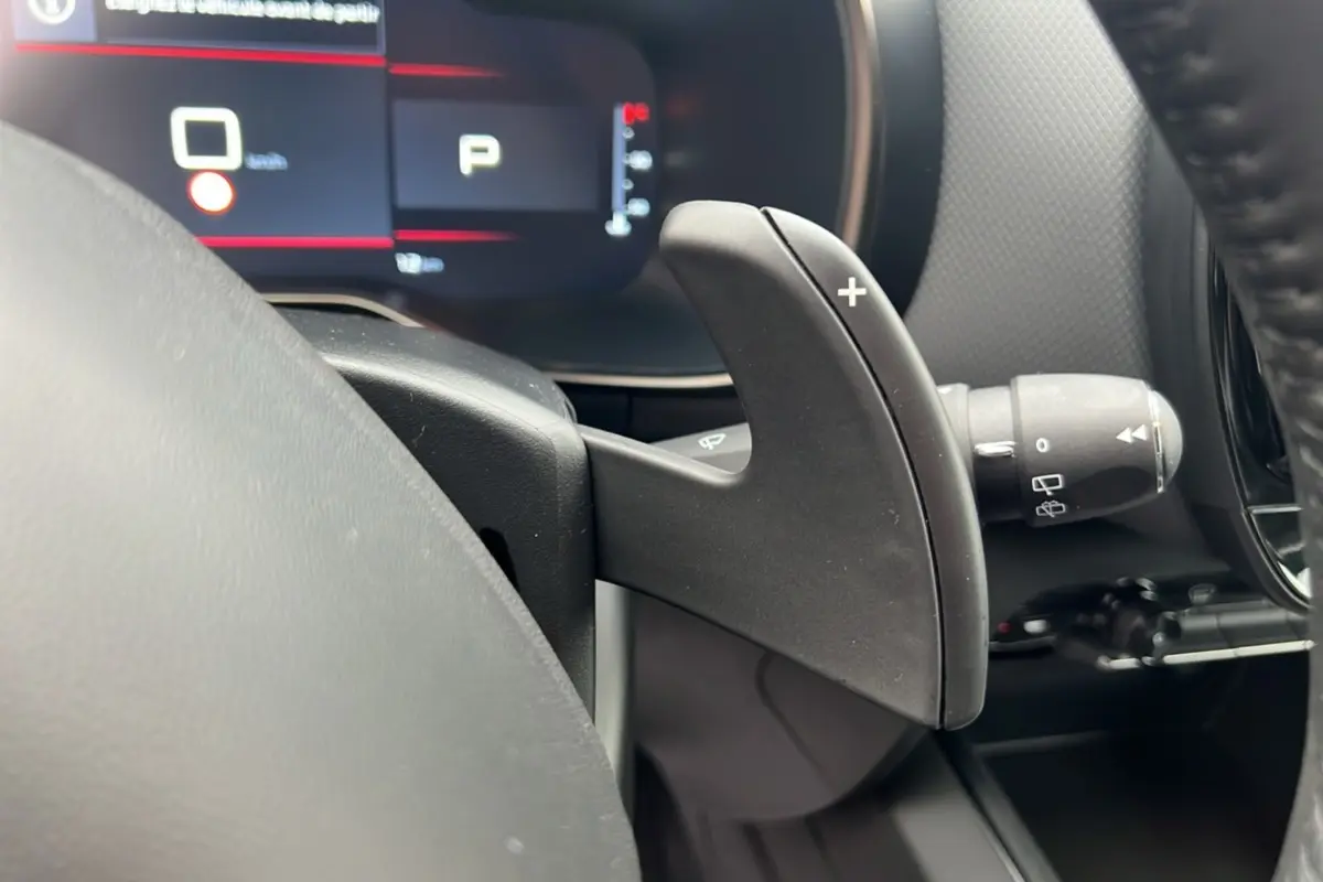 Gros plan sur la palette de passage de vitesses droite du Citroën C5 Aircross Hybrid 2025, tableau de bord numérique en arrière-plan.