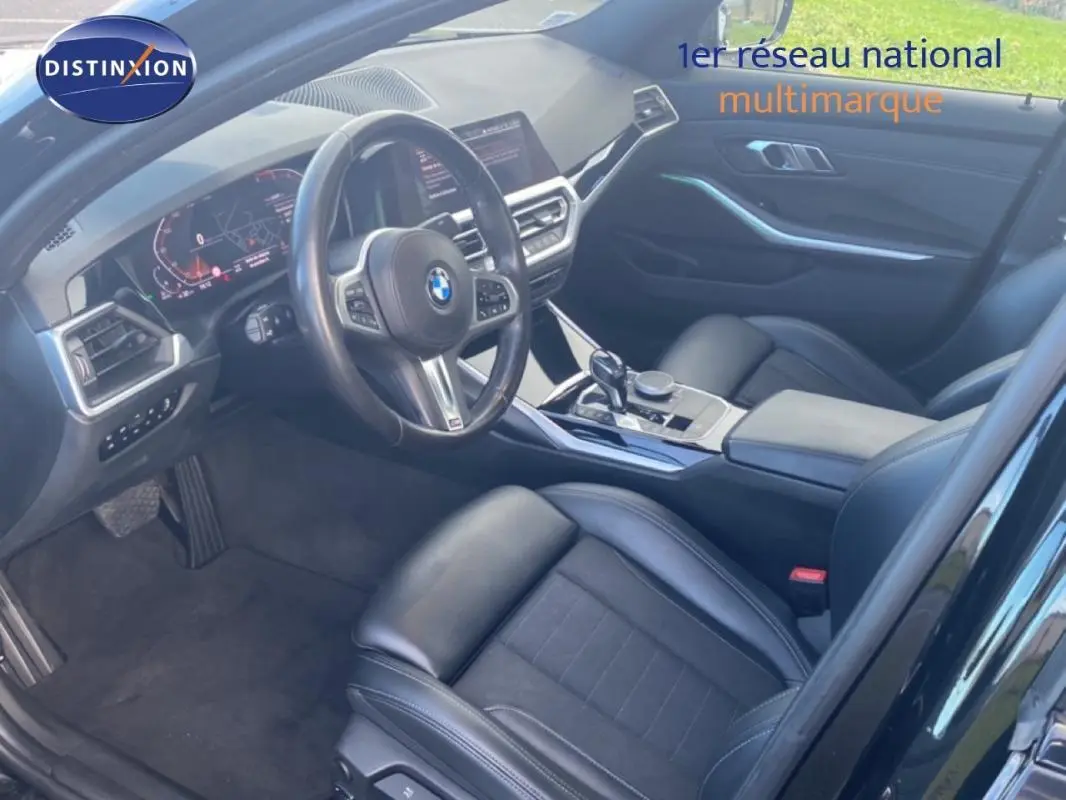 Vue intérieure côté conducteur de la BMW Série 3 G20 noire, avec volant sport, console centrale et sièges en cuir noir.