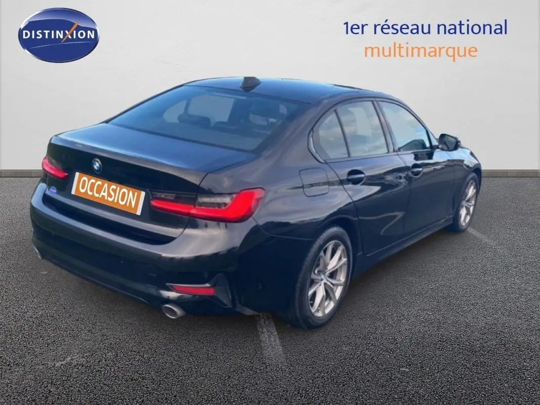 BMW Série 3 G20 noire vue 3/4 arrière droit, avec jantes alliage 17 pouces et feux arrière allumés.