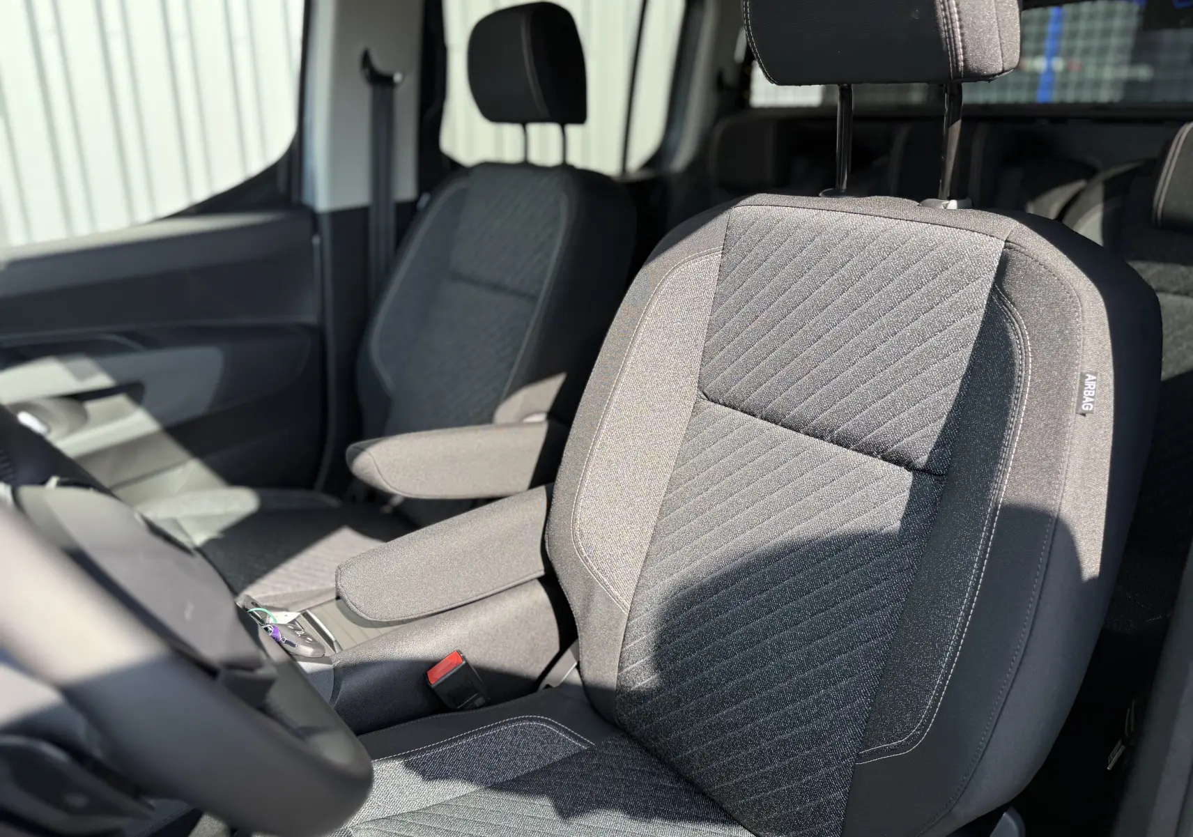 Vue intérieure rapprochée des sièges avant gris foncé du Peugeot Rifter Allure 2026 avec accoudoirs et étiquette airbag visible.