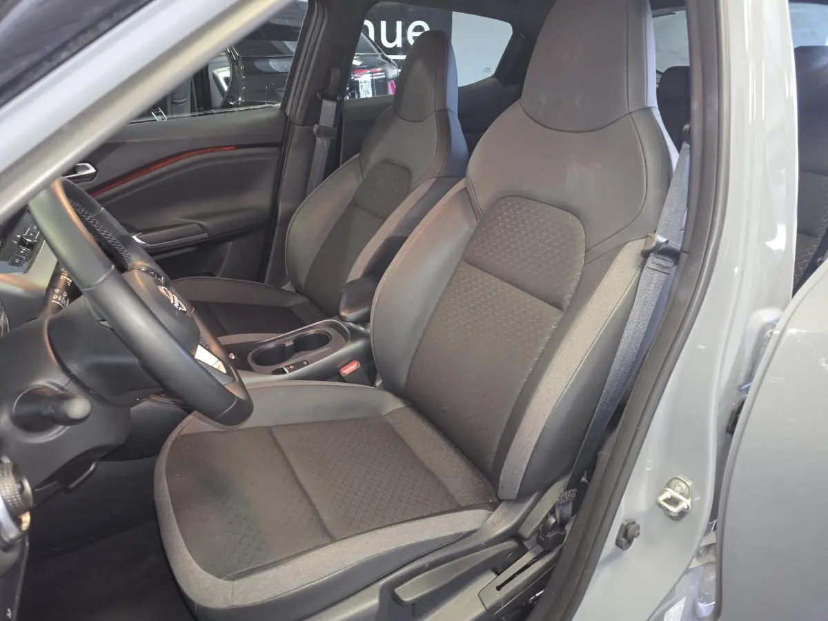 Vue intérieure côté conducteur du Nissan Juke 2025 gris, montrant les sièges avant en tissu et TEP noir et gris avec accoudoir central.